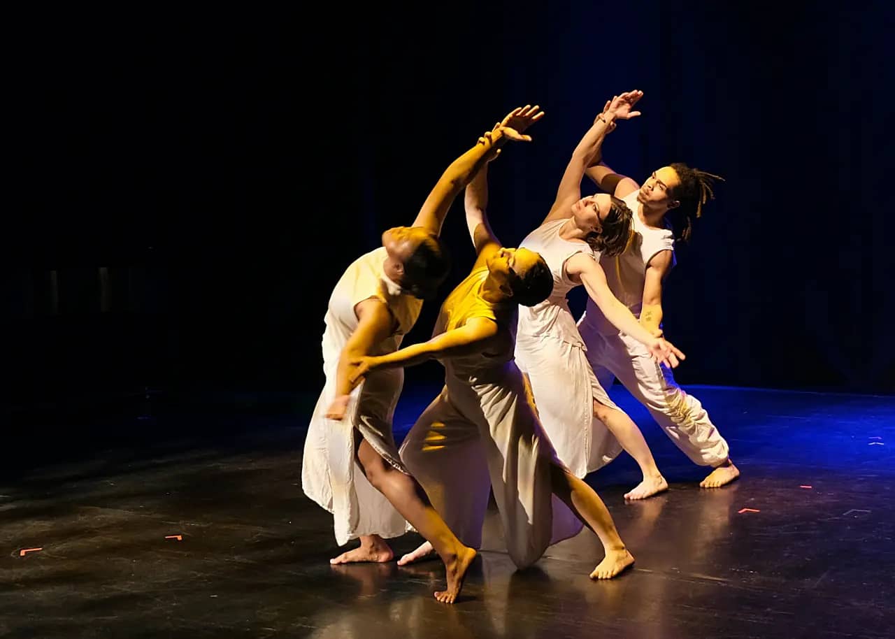 Four dancers in white performing on stage.